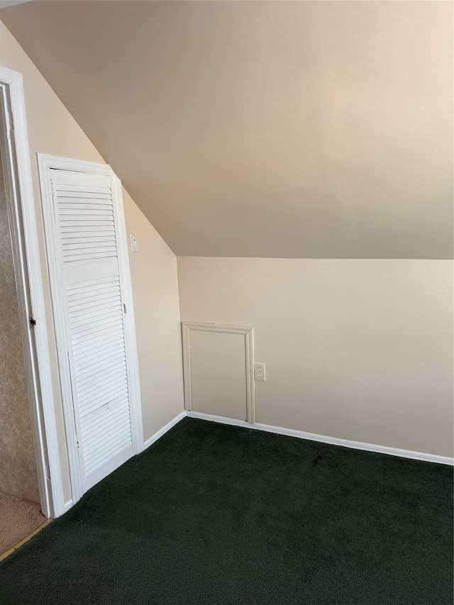 additional living space with dark colored carpet, lofted ceiling, and baseboards