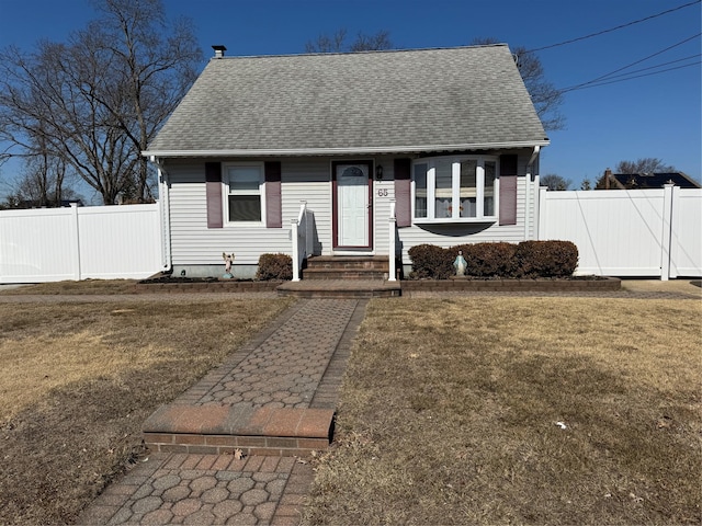 view of front facade featuring a front yard, fence, and roof with shingles