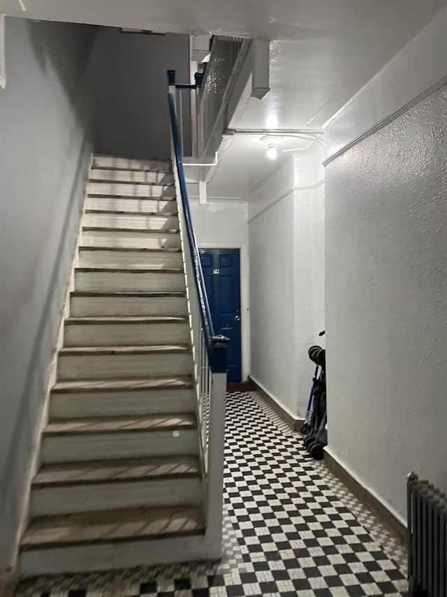 staircase featuring radiator, a textured wall, baseboards, and tile patterned floors