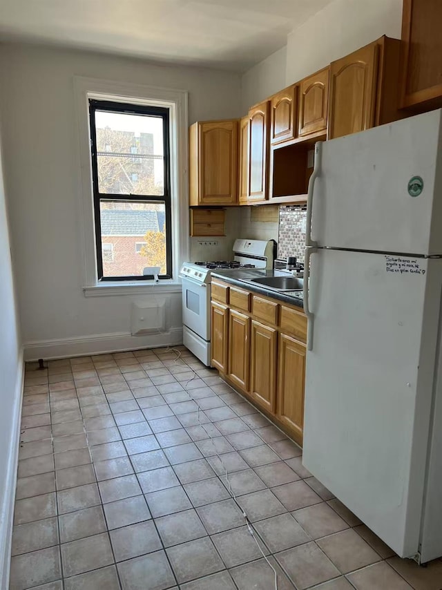 kitchen featuring light tile patterned floors, white appliances, baseboards, backsplash, and dark countertops