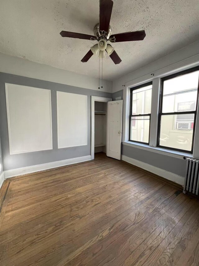 unfurnished bedroom with a textured ceiling, wood finished floors, baseboards, a closet, and radiator