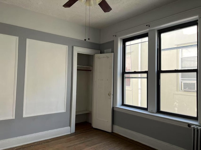 unfurnished bedroom with baseboards, radiator heating unit, wood finished floors, a textured ceiling, and a closet