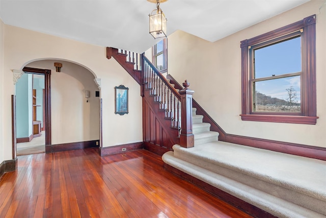 foyer with arched walkways, dark wood-style flooring, stairway, and baseboards