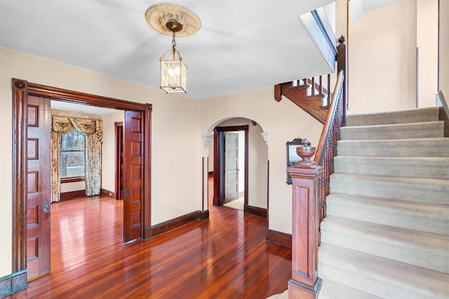 foyer entrance featuring arched walkways, stairway, wood finished floors, and baseboards