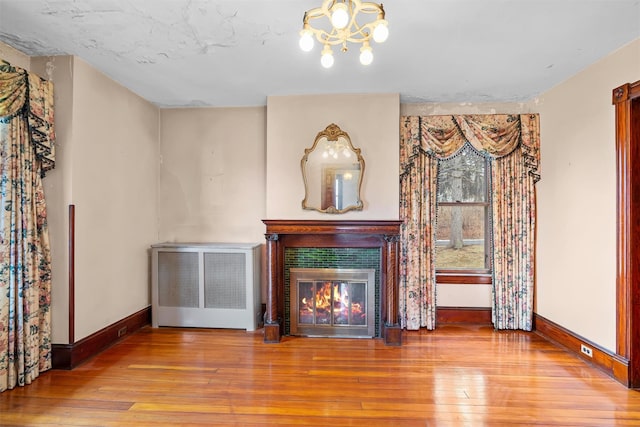 unfurnished living room featuring a glass covered fireplace, wood-type flooring, radiator, and baseboards