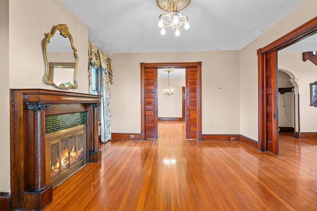 interior space with baseboards, arched walkways, a tile fireplace, hardwood / wood-style floors, and a notable chandelier