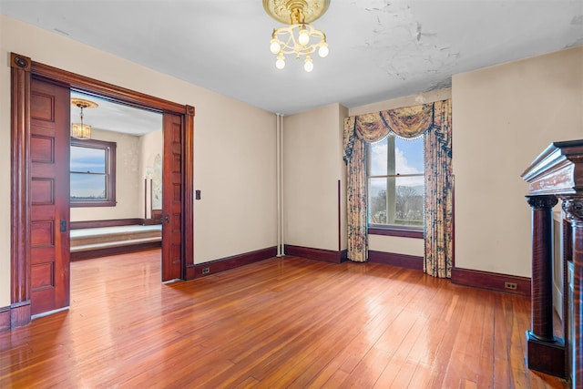 unfurnished living room with a chandelier, wood-type flooring, and baseboards