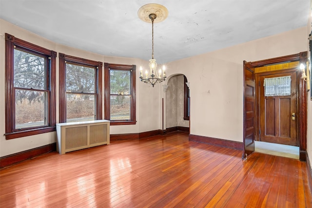 unfurnished dining area featuring arched walkways, radiator, a notable chandelier, and hardwood / wood-style floors