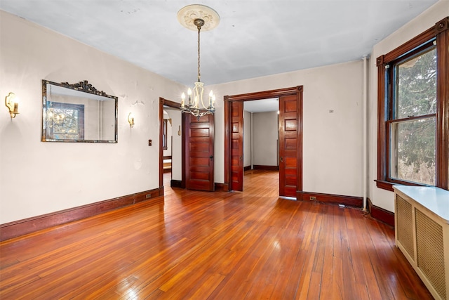 unfurnished room with hardwood / wood-style flooring, radiator heating unit, a chandelier, and baseboards