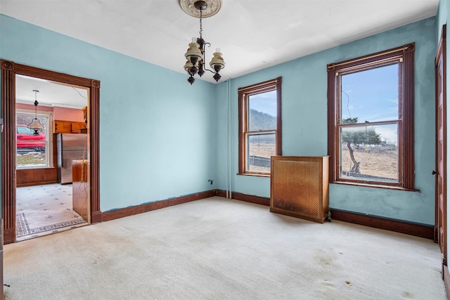 carpeted empty room featuring baseboards and an inviting chandelier