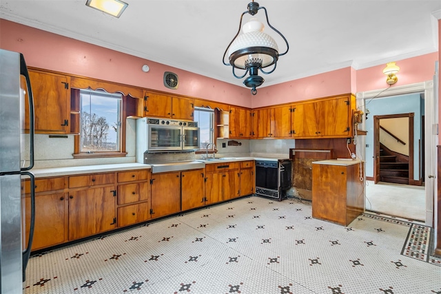 kitchen featuring brown cabinets, crown molding, stainless steel appliances, light countertops, and a sink