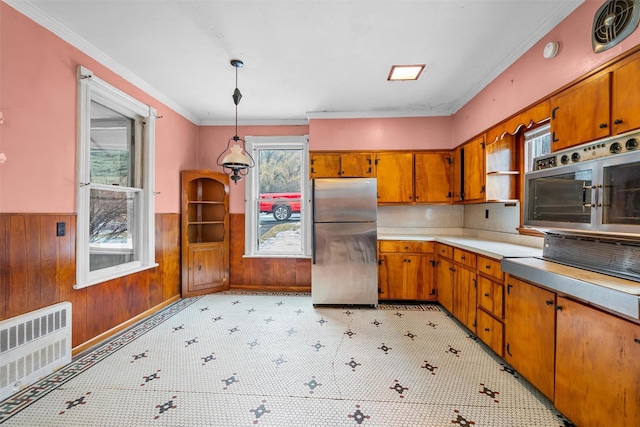 kitchen featuring wood walls, appliances with stainless steel finishes, wainscoting, brown cabinets, and radiator