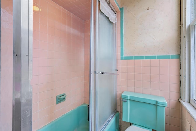 full bathroom with toilet, combined bath / shower with glass door, wainscoting, and tile walls