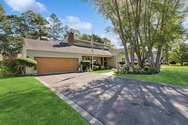 view of front of house with an attached garage, driveway, a chimney, and a front yard