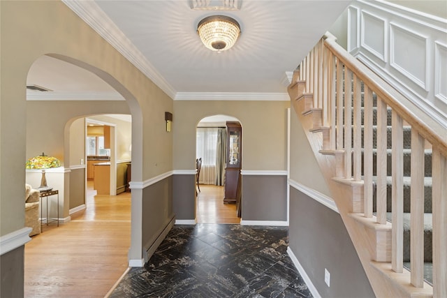 foyer entrance with arched walkways, visible vents, baseboard heating, ornamental molding, and baseboards