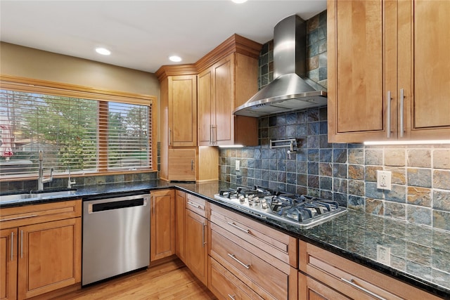 kitchen with light wood-style flooring, stainless steel appliances, a sink, wall chimney range hood, and backsplash