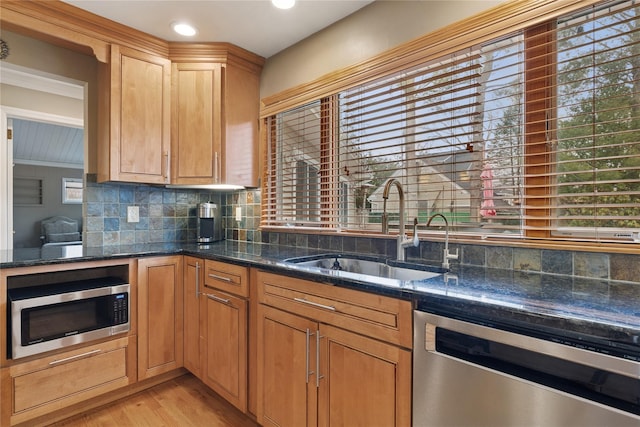 kitchen with appliances with stainless steel finishes, backsplash, a sink, and dark stone counters