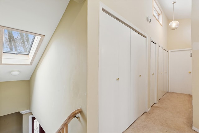 hall with a high ceiling, a skylight, and light colored carpet