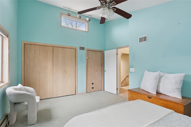 bedroom featuring carpet, visible vents, baseboard heating, and two closets