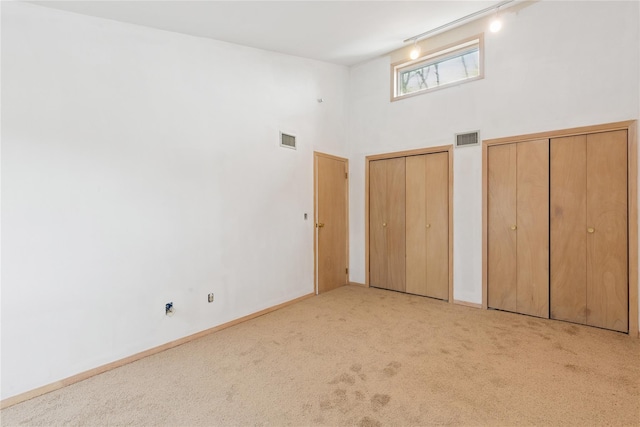 unfurnished bedroom with light carpet, track lighting, visible vents, and two closets