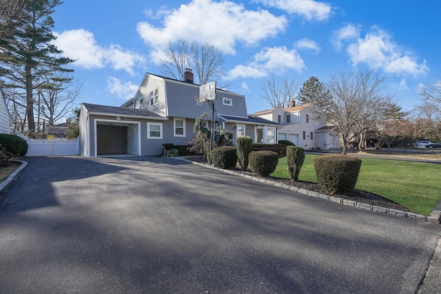 colonial inspired home with aphalt driveway, an attached garage, fence, a gambrel roof, and a front yard