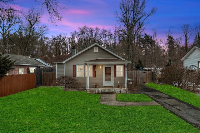 bungalow-style home with driveway, fence, a chimney, and a front lawn