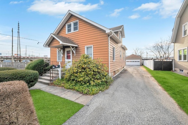 bungalow featuring a shingled roof, a detached garage, fence, an outdoor structure, and a front lawn