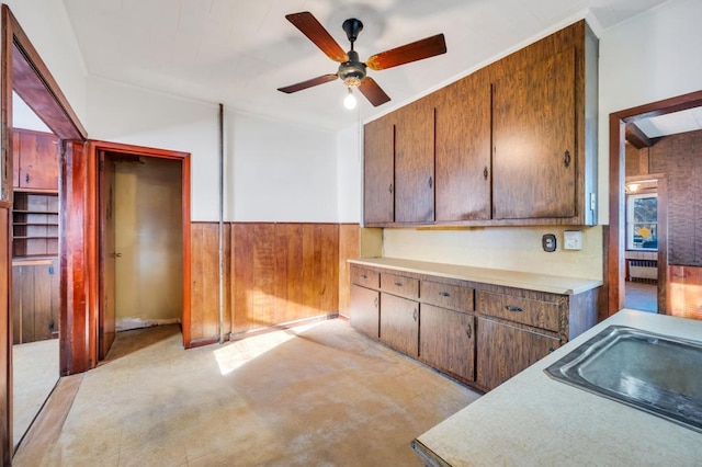 kitchen with a wainscoted wall, radiator, light countertops, a sink, and wooden walls