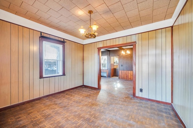 unfurnished room featuring a chandelier, wooden walls, and baseboards