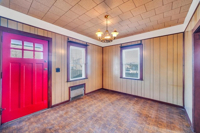 empty room featuring radiator, wooden walls, baseboards, and a notable chandelier