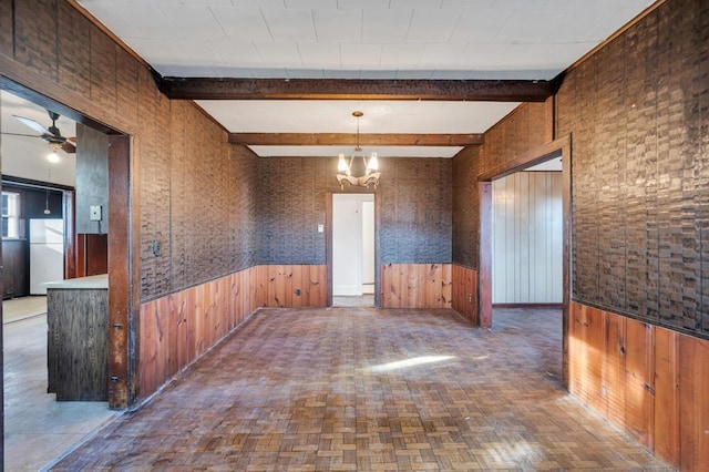 empty room with a wainscoted wall, beamed ceiling, and ceiling fan with notable chandelier