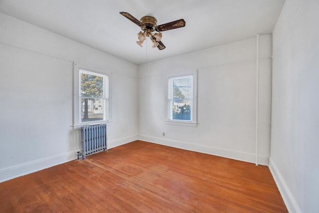 empty room featuring a ceiling fan, plenty of natural light, hardwood / wood-style flooring, and radiator