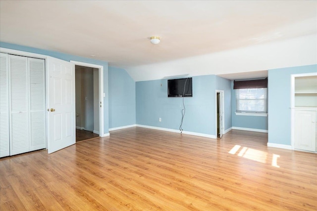 unfurnished bedroom featuring lofted ceiling, light wood-style flooring, and baseboards