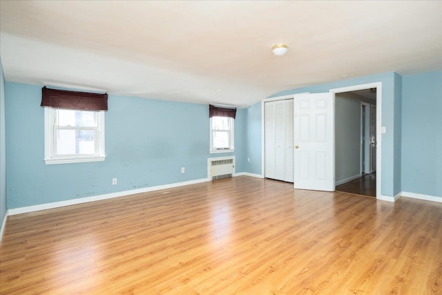 spare room featuring light wood finished floors, radiator heating unit, and baseboards