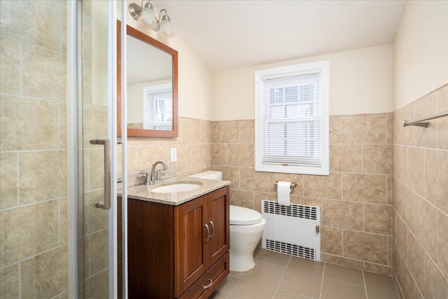 full bathroom with a stall shower, radiator, toilet, vanity, and tile walls