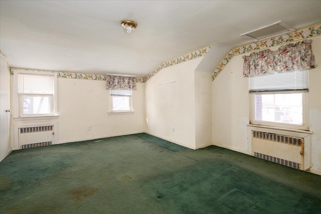 empty room featuring attic access, dark colored carpet, and radiator