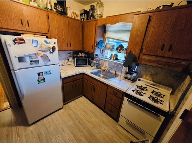 kitchen featuring white appliances, decorative backsplash, light wood-style flooring, light countertops, and a sink