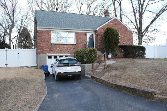 view of front of home with driveway, a shingled roof, a chimney, a gate, and brick siding