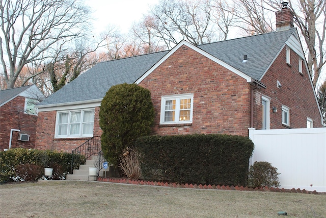 view of side of home featuring a shingled roof, brick siding, a lawn, and a chimney