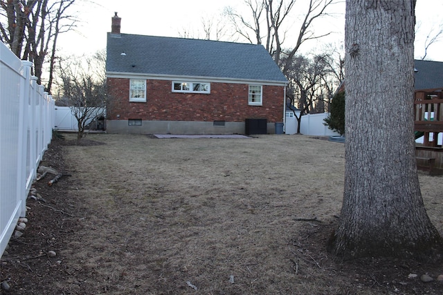 rear view of house with a fenced backyard, brick siding, roof with shingles, crawl space, and a chimney