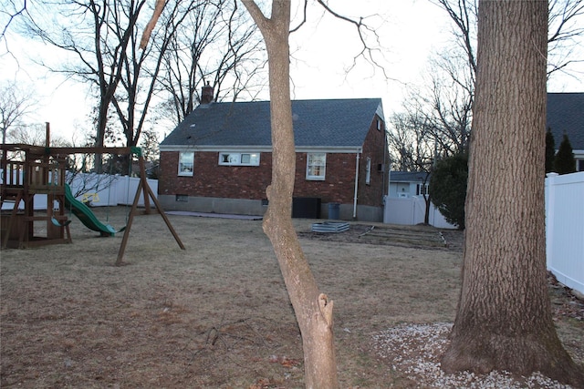 rear view of property featuring a fenced backyard, a chimney, roof with shingles, a playground, and brick siding