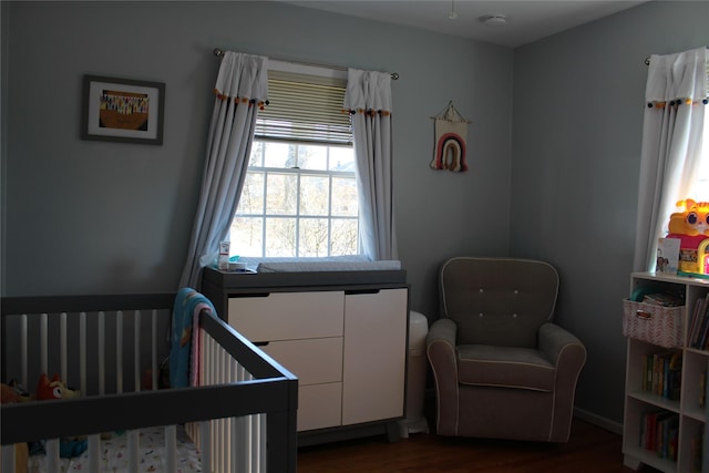 bedroom with a nursery area and dark wood-style flooring