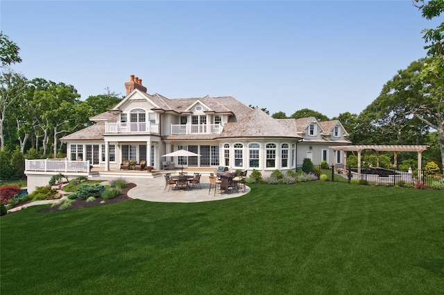 back of property with a balcony, a chimney, fence, a yard, and a pergola