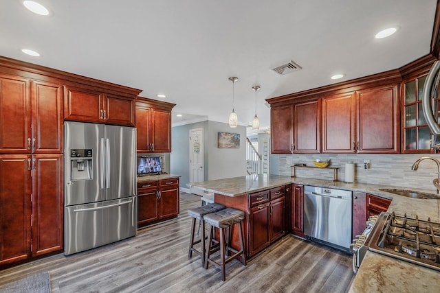 kitchen with reddish brown cabinets, visible vents, stainless steel appliances, and a sink