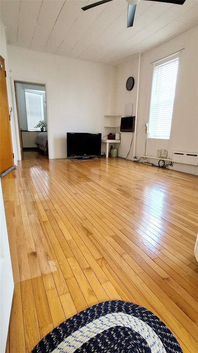 unfurnished living room featuring ceiling fan, baseboard heating, and hardwood / wood-style flooring