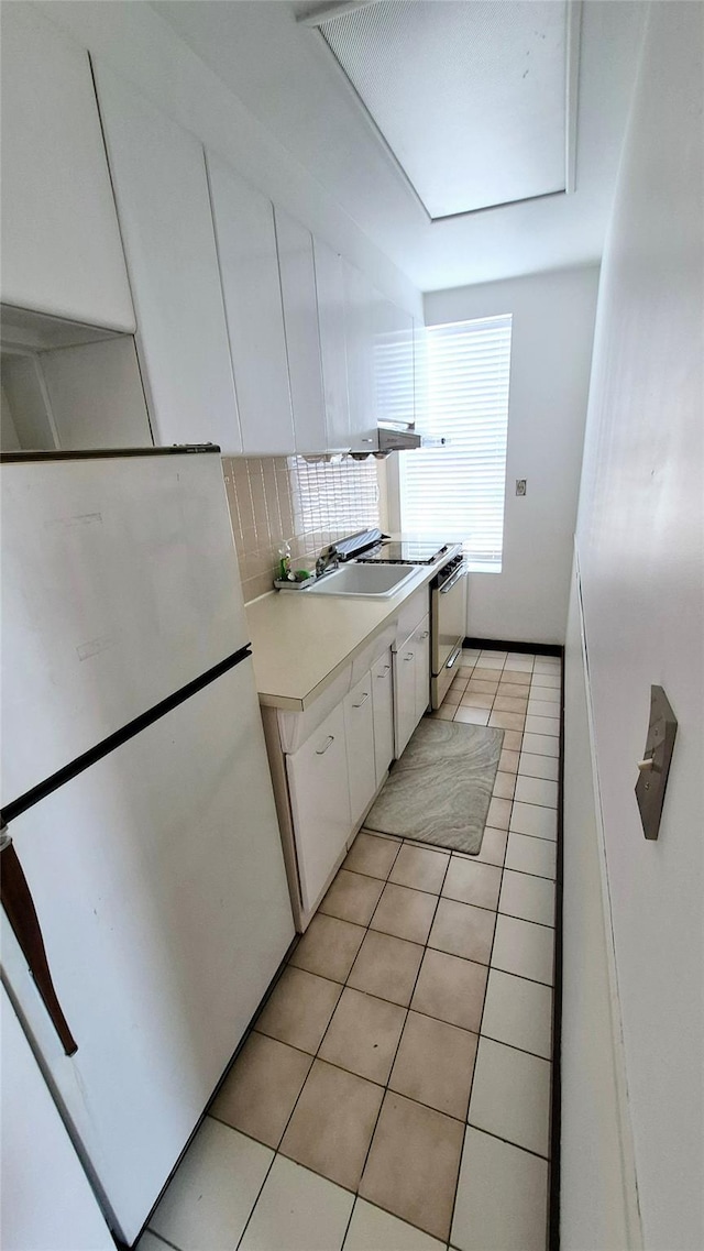 kitchen featuring light tile patterned floors, freestanding refrigerator, light countertops, white cabinetry, and a sink