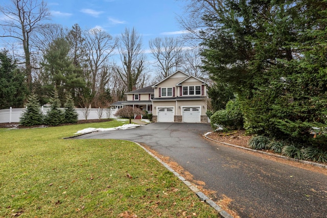 view of front of home with driveway, stone siding, an attached garage, fence, and a front yard