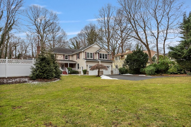 back of property with a yard, a chimney, an attached garage, fence, and driveway