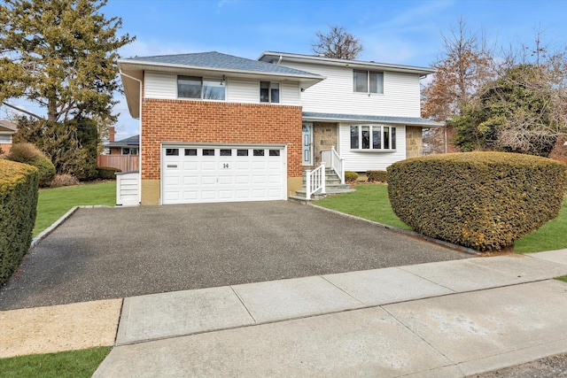 split level home featuring a garage, aphalt driveway, fence, a front lawn, and brick siding