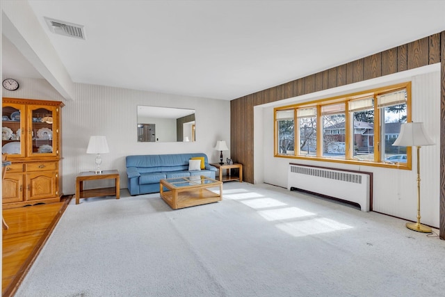 carpeted living area featuring wood walls, visible vents, and radiator